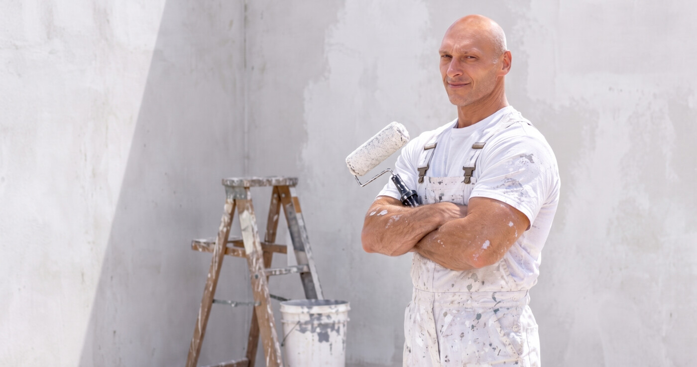 Dumitru Grecu, painter and decorator in Galway, standing with arms crossed holding a paint roller